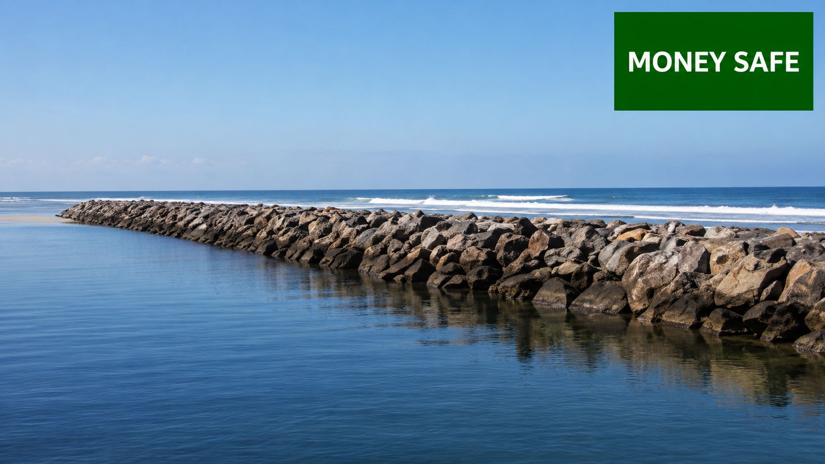 A long stone jetty extending into the calm blue ocean under a clear bright sky.